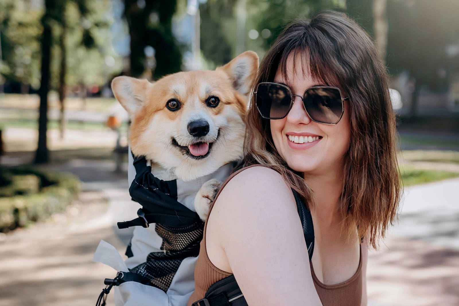 Female with sunglasses and short brown hair carrying a Corgi on her back