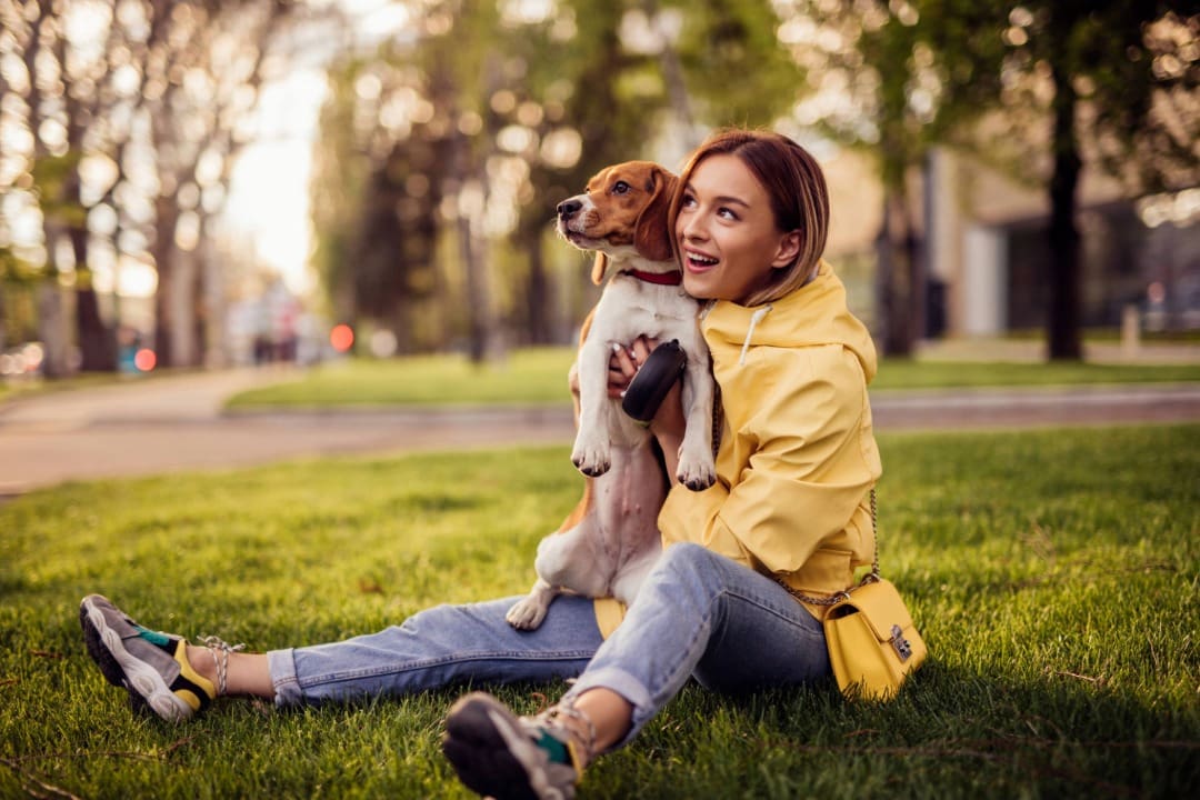 Female wearing a yellow raincoat sitting in grass holding a Beagle