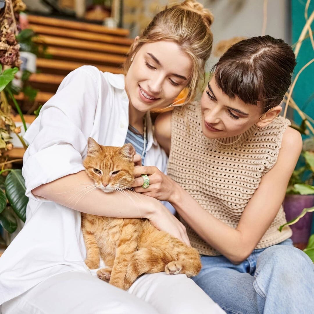 2 females sitting on a bench holding an orange tabby cat